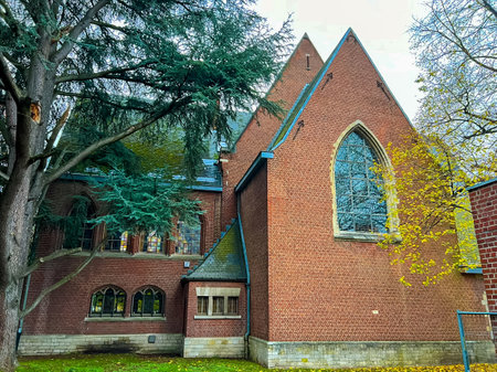 A striking gothic style red brick church stands majestically, framed by lush green trees. The image is captured from the street, showcasing its intricate architecture and serene surroundings.の写真素材