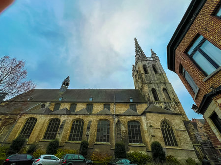 This photograph captures the stunning exterior of a church in Leuven, viewed from below. The overcast sky creates a dramatic backdrop, enhancing the architectural details of the church.の写真素材