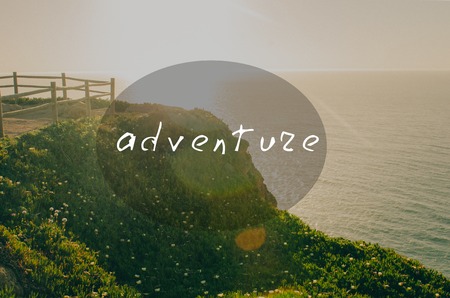 Beautiful sunset view to green mountain with flowers and wooden fence near ocean. Oval insert with adventure signの写真素材