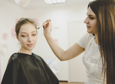 Beautiful young professional woman tweezing shirtless woman eyebrows Mikrobleyding eyebrows workflow in a beauty salonの写真素材