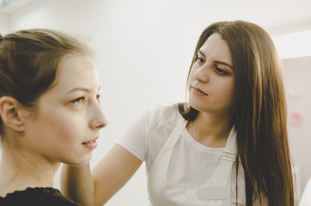 Beautiful young professional woman tweezing shirtless woman eyebrows Mikrobleyding eyebrows workflow in a beauty salonの写真素材