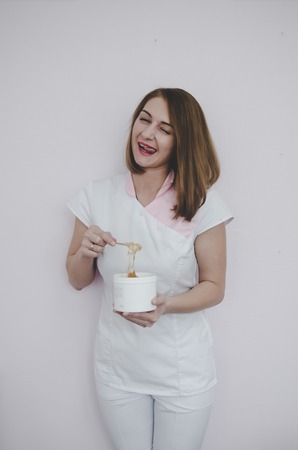 beautiful young woman standing near white wall with hair removal wax in hands and smilingの写真素材