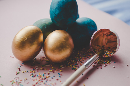 Beautiful colorful blue and golden easter eggs with confectionery sprinkling and brush on pink backgroundの写真素材