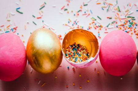 Beautiful colorful pink and golden easter eggs with confectionery sprinkling and brush on pink backgroundの写真素材