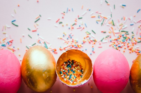 Beautiful colorful pink and golden easter eggs with confectionery sprinkling and brush on pink backgroundの写真素材