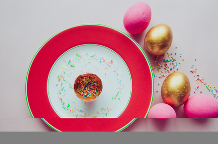 Beautiful colorful pink and golden easter eggs with confectionery sprinkling on plate and pink backgroundの写真素材