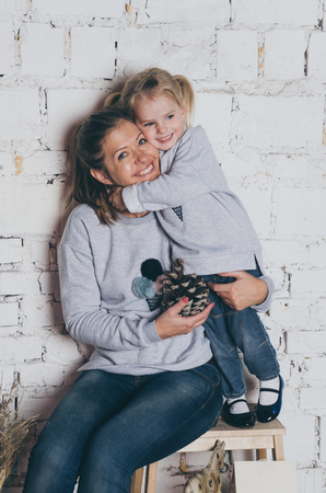 young mother and little daughter in same clothes standing near white wall and huggingの写真素材