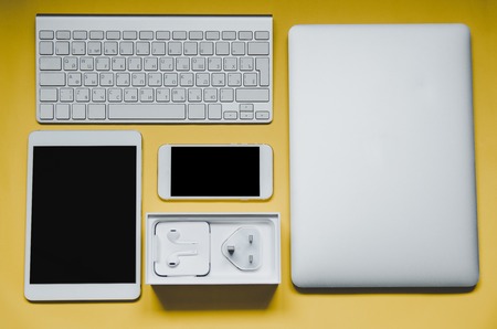 keyboard,touch pad, smartphone, laptop and charger on yellow background, top viewの写真素材
