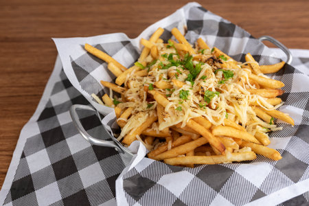 French fries with cheese and parsley on a napkin on a wooden background