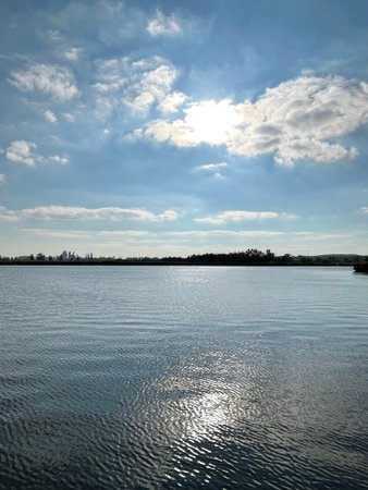 Sunlight Glittering on Calm Lake with Skyline in Distance Serene Nature Meets Urban Landscapeの写真素材