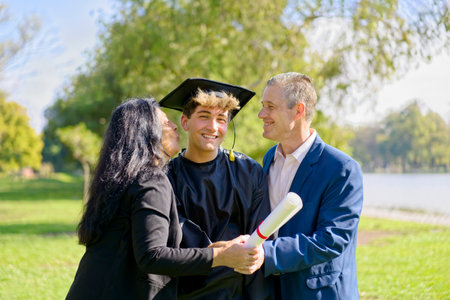 Young recently graduated boy, dressed in cap and gown, with his degree in hands, celebrating with his multi ethnic  family on the university campus. Very happy expression, achievementの写真素材