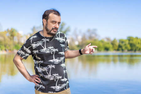 Bearded mature man in a lake looking at the camera with one arm akimbo and the other pointing to the side. copy-spaceの写真素材