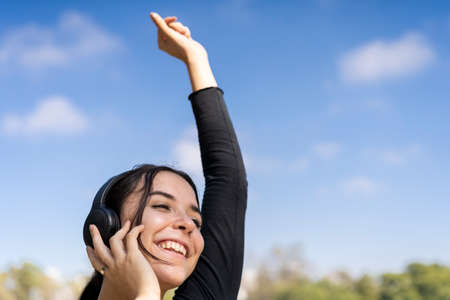 Young woman listening to music outdoors with headphones. Expression of happiness, winning attitude....