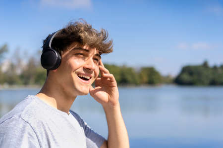 Young man listening to music outdoors with headphones. Expression of happiness, winning attitude.