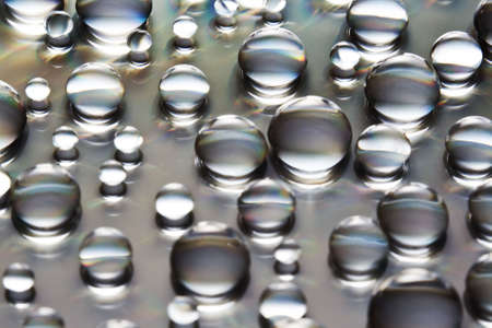 Water Drops in a variety of sizes over a grayish reflective background. Shallow D.O.F.