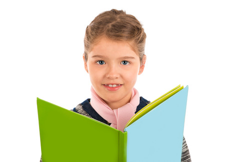 A cute little girl holding a big storybook looking at the camera and smiling  Isolated on white の写真素材
