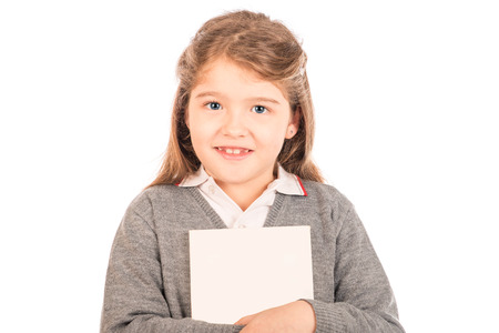 A small girl wearing a gray school uniform hugging a blanked out book looking at the camera  Isolated on white の写真素材