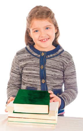 Little girl looking at the camera smiling with a pile of closed books on a table  Isolated on white の写真素材