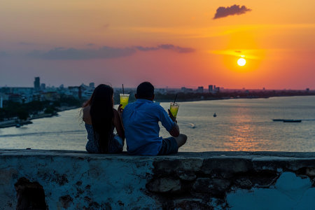 Couple drinking cocktails and watching the sunset on the roof of the buildingの素材