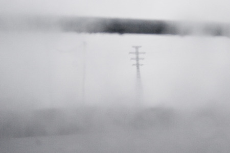 Power lines in fog through a wet window in gray tones