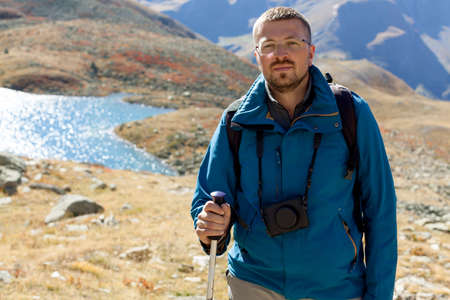 Trendy hipster portrait of man outdoor for healthy lifestyle design. Trekking of blogger photographer or vlogger with camera. Solo tourist in the Alpsの写真素材