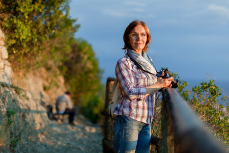 Close up portrait of lovely middle aged woman with dslr photo camera. Attractive thoughtful mature woman leaning resting on fence in the countryside. Solo domestic isolation tourismの写真素材