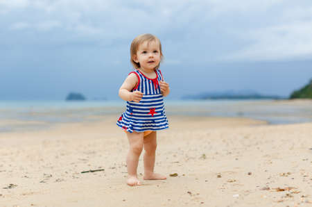 Toddler baby doing her first steps on sand near the bank. Little cute girl playing on the beach. Small child enjoying vacation by the sea or ocean. Travelling with kids concept. Photo with copy spaceの写真素材