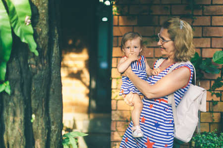 Happy grandmother lifting up her little granddaughter and hugging in garden at sunny day outdoors....