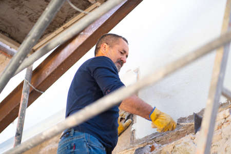 Construction worker on a ladder fixing a wall