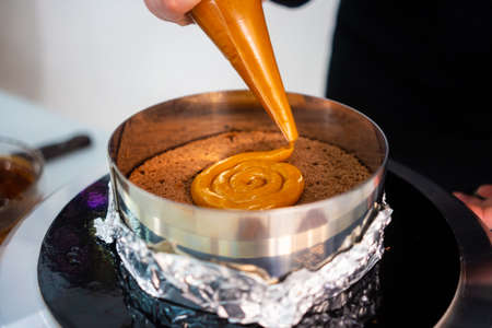 Pastry chef decorating a delicious cake with a caramel piping bag.の写真素材