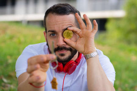 Young man posing with new home key and bitcoin coin. Young investor concept.