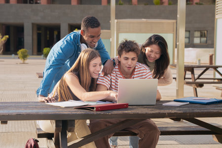 A group of students with laptops sit near the campus and communicate.