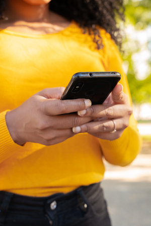 Vertical Close-up image of the hands of a young African American woman browsing the internet outdoors.の写真素材