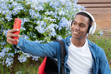 Young African American man taking a selfie with cell phone and smiling outdoors.の写真素材