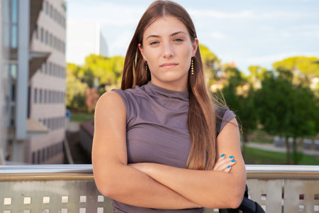 portrait Young serious caucasian student woman with arms crossed looking thoughtful outdoors.の写真素材