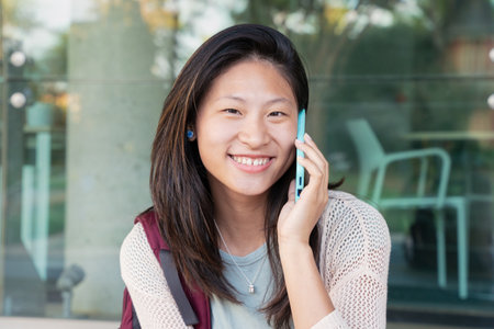 young asian woman sitting having friendly conversation on smartphone outdoor.の写真素材