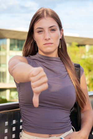 Vertical portrait Young angry caucasian woman pointing thumb down looking thoughtful outdoors.