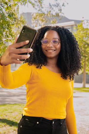Vertical portrait African American woman smiling taking a photo of herself with a smartphone outdoors.の写真素材