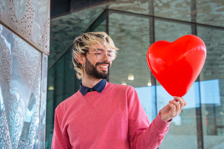 Smiling young man standing holding a heart-shaped balloon. Loveの写真素材