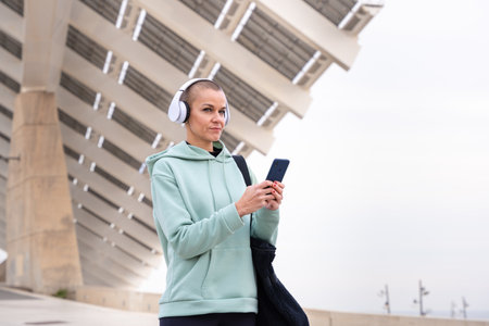 A smiling female runner takes a break to use an app on her smartphone outdoors.