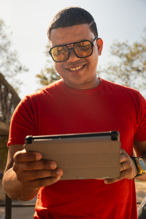 Vertical portrait glamorous smiling young man, sitting using a app on a digital tablet outdoors.の写真素材