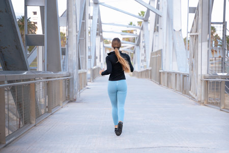 Rear view a young runner with water bottle in hand trains around the city.の写真素材