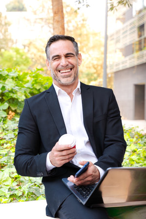 Smiling businessman with laptop and smartphone outdoorsの写真素材