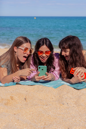 Three happy young friends on the beach using apps on their smartphones.Verticalの写真素材