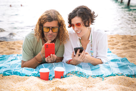 Smiling couple on the beach browsing smartphone apps.の写真素材