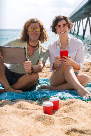 Vertical portrait smiling couple on the beach browsing smartphone apps.の写真素材