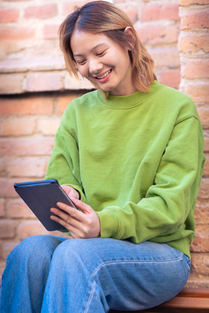 Smiling young asian woman sitting surfing the internet on a digital tablet.