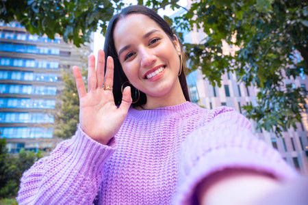 Latin woman having a video call with cell phone and smiling outdoors.