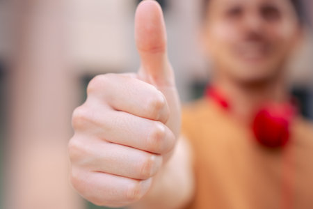 Young Caucasian man pointing thumb up looking smiling at camera outdoors.の写真素材
