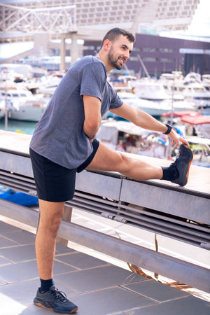 Active and fit male runner in warm-up stretch for running or cardio exercise.